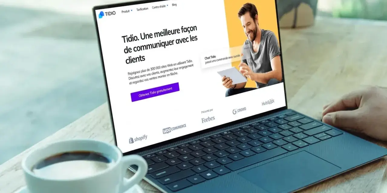 Un homme souriant utilise un logiciel de chat gratuit sur une tablette, montrant une interface de communication client sur un ordinateur portable.