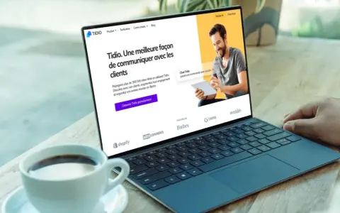 Un homme souriant utilise un logiciel de chat gratuit sur une tablette, montrant une interface de communication client sur un ordinateur portable.