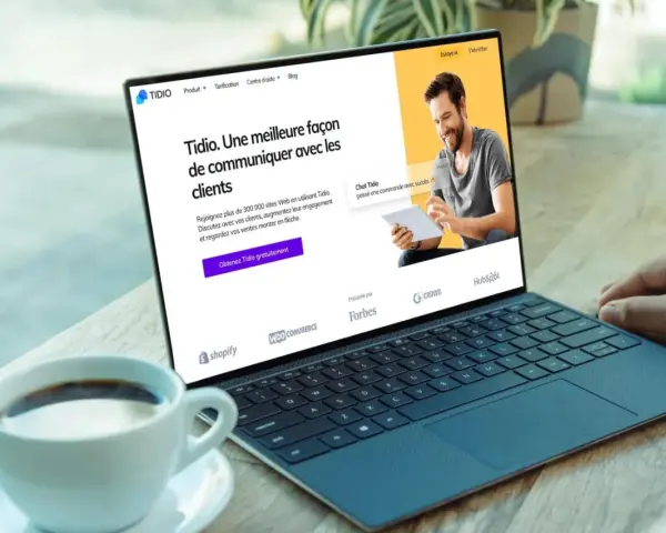 Un homme souriant utilise un logiciel de chat gratuit sur une tablette, montrant une interface de communication client sur un ordinateur portable.