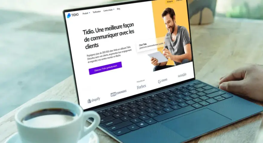 Un homme souriant utilise un logiciel de chat gratuit sur une tablette, montrant une interface de communication client sur un ordinateur portable.
